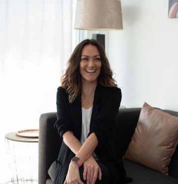 Marisa, founder of The Five, sitting on a couch and smiling